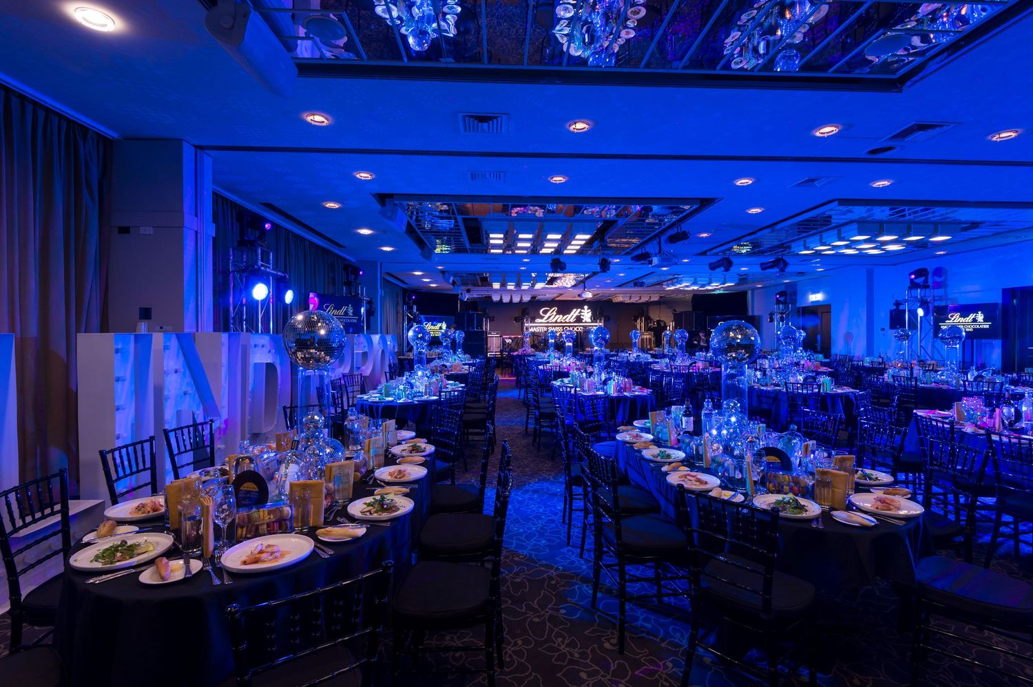 A luxurious banquet hall decorated with blue uplighting and elegant table settings for an evening event.