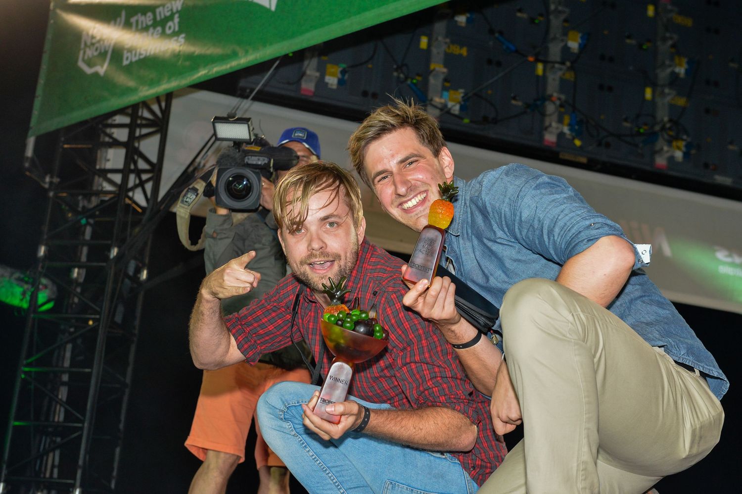 Two people posing playfully with drinks at a nightclub with green lighting in the background.