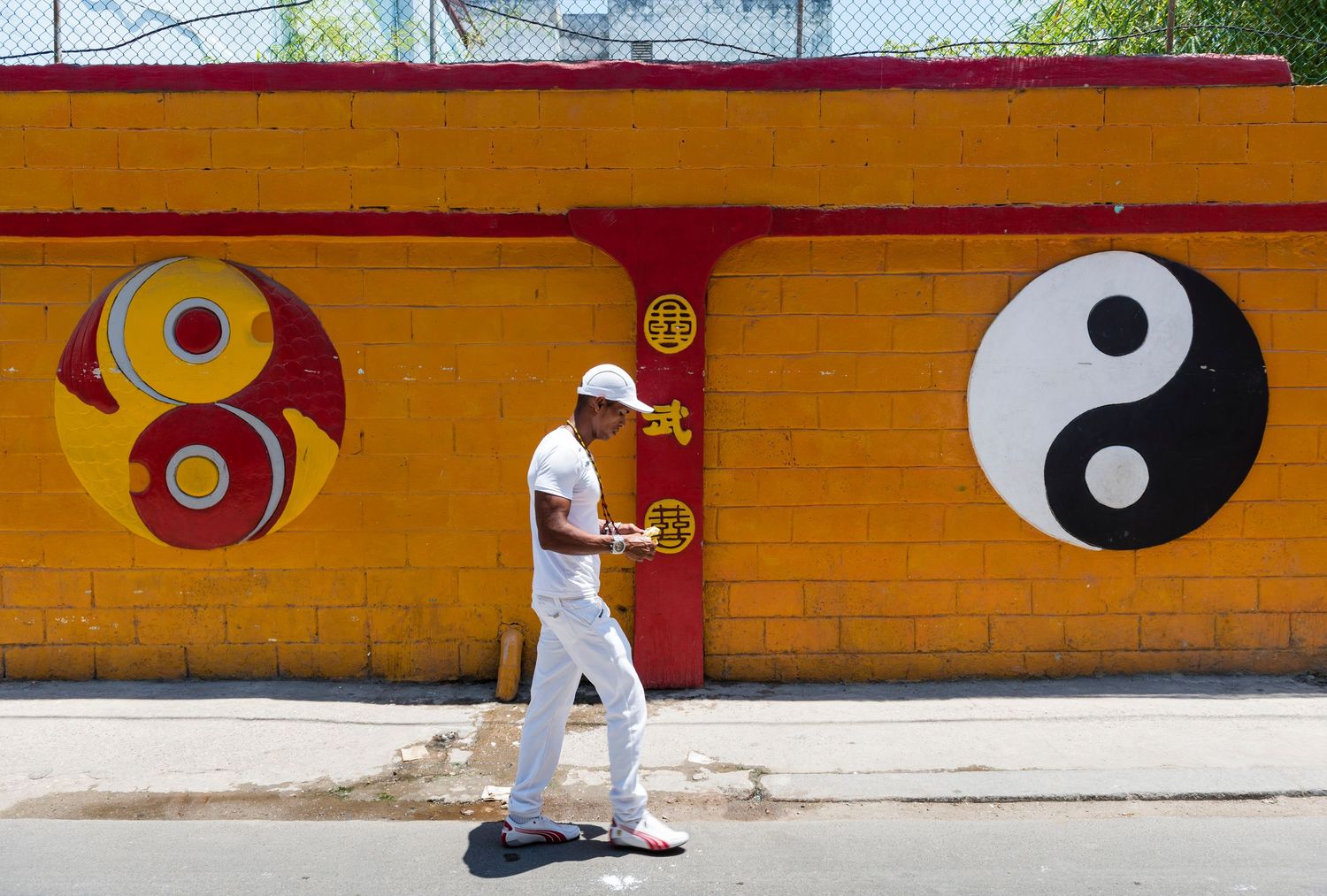 Person in white walks past orange wall with yin yang symbols painted on it.