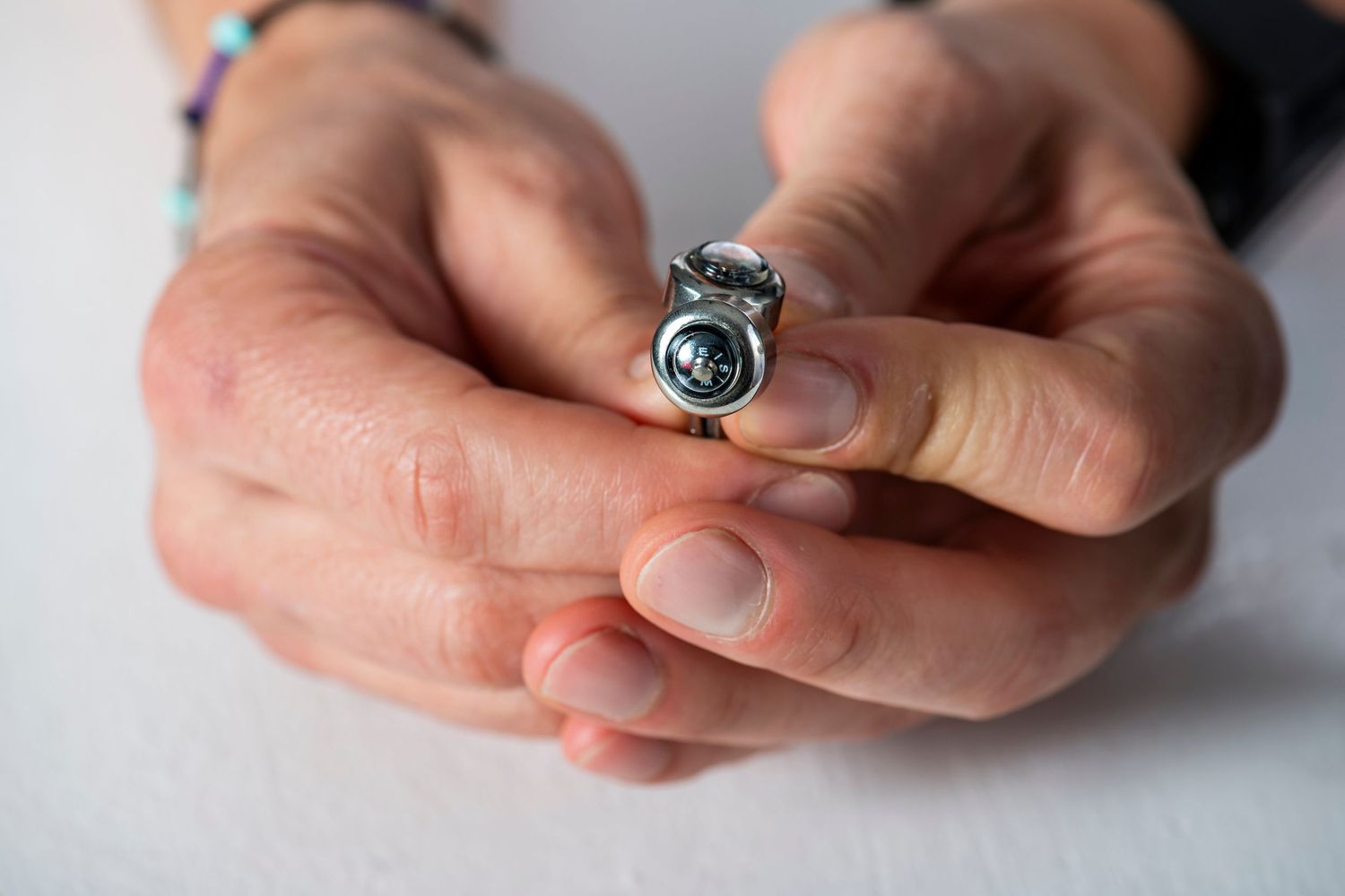 Close-up view of hands holding and examining small jewelry pieces on a white surface.