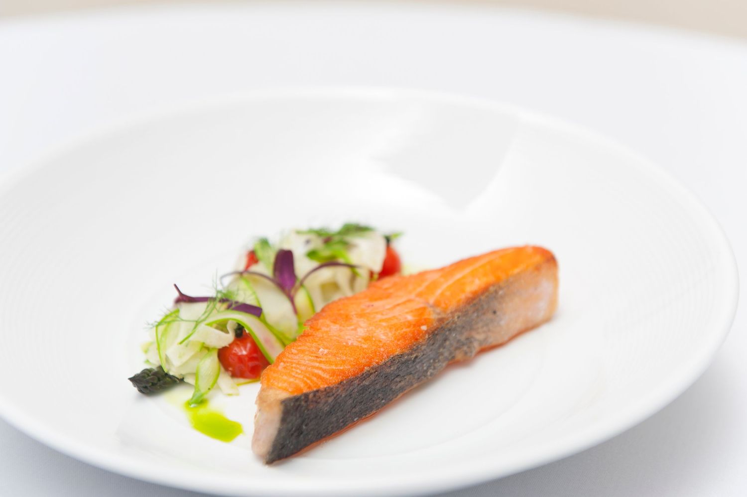 Perfectly cooked salmon fillet plated elegantly with microgreens on a white dish.