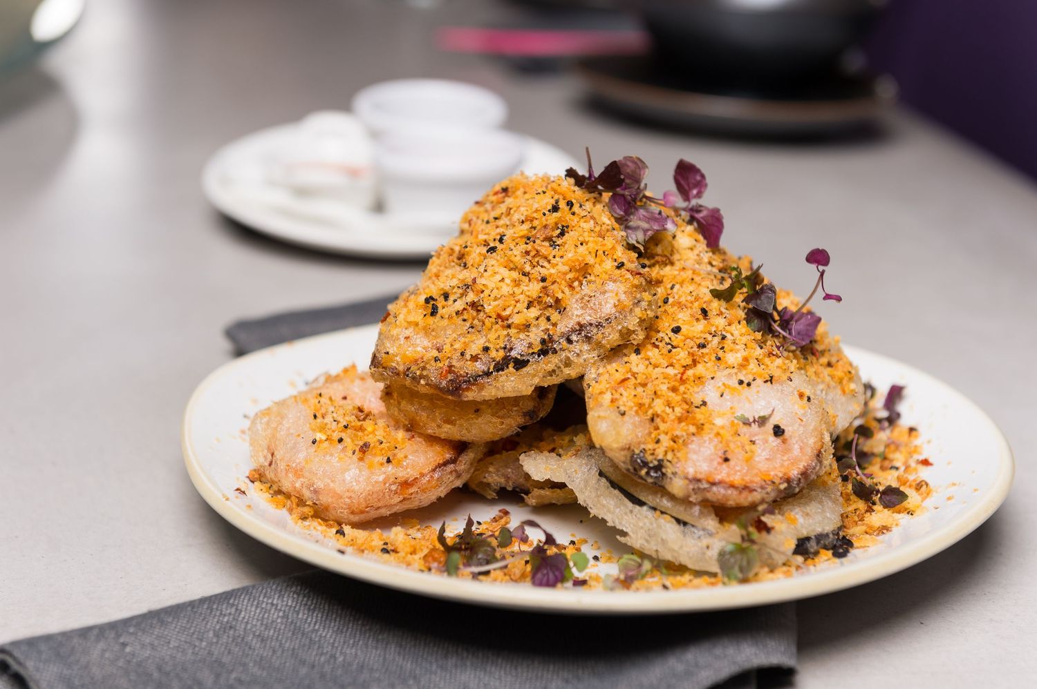 Pan-seared scallops with golden crust and microgreen garnish on white plates.