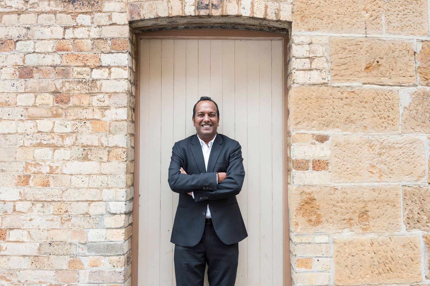 Professional in business suit stands with crossed arms against beige doorway.