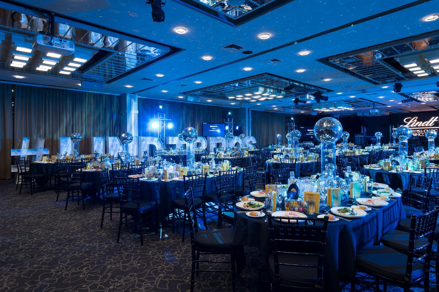 Large modern ballroom with blue uplighting and round tables set for an elegant evening event.