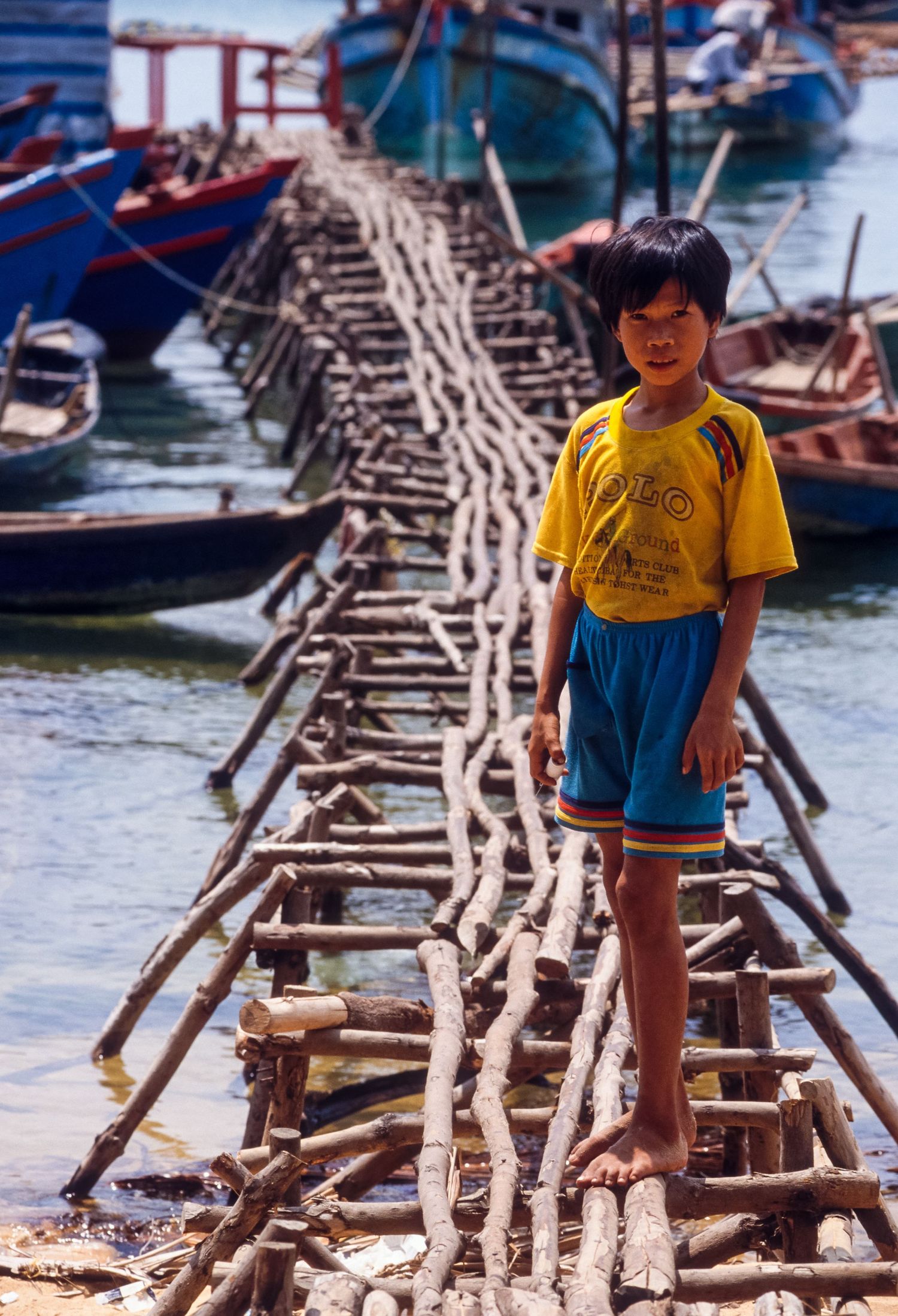 Wooden walkway made of bamboo poles stretches across water at a floating market in Vietnam.