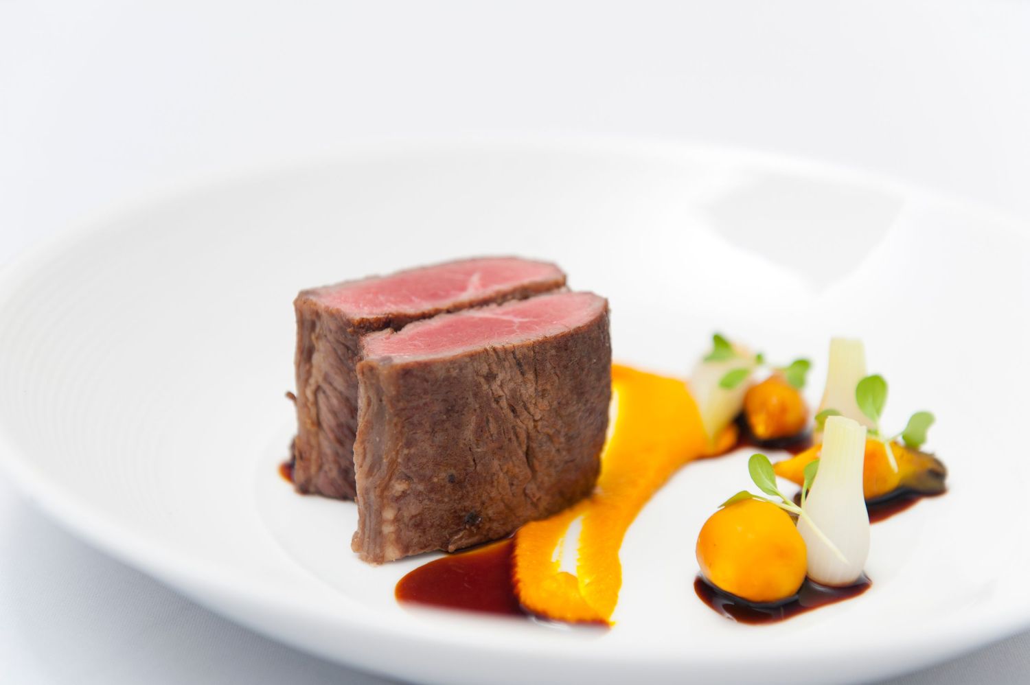 Medium-rare beef tenderloin served with colorful citrus elements and sauce on white plate.