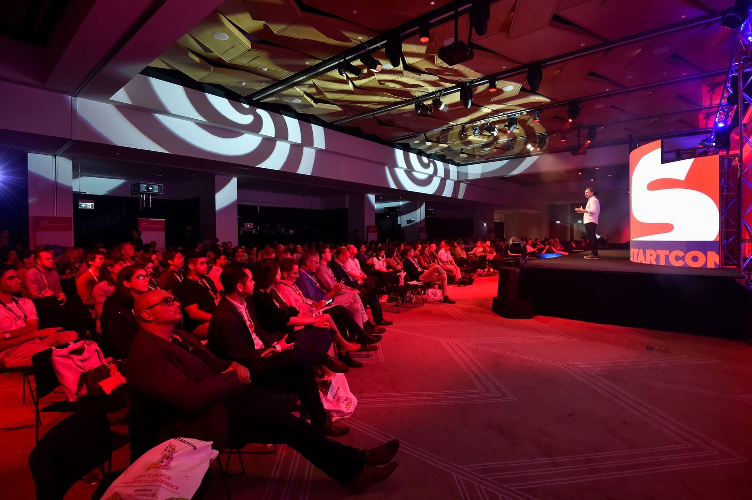 Conference attendees seated in rows at an event in Sydney Royal Randwick with dramatic red lighting and projected visuals.