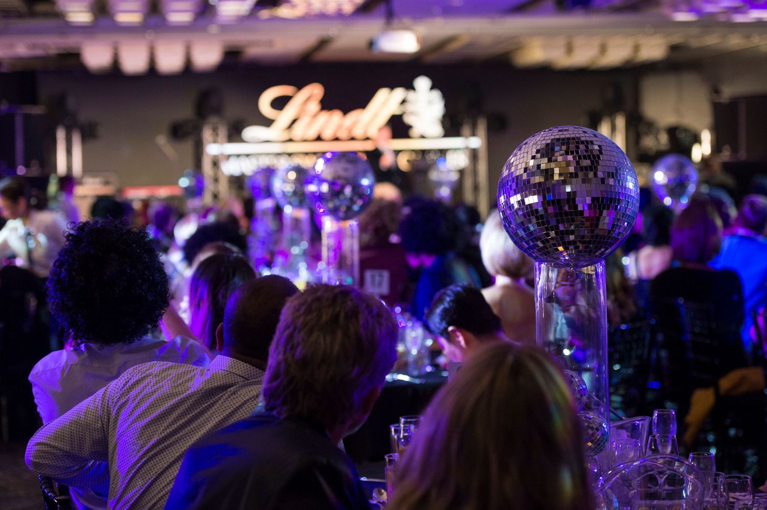 Dimly lit event space with purple and blue lighting illuminating a crowded room during a formal gathering.