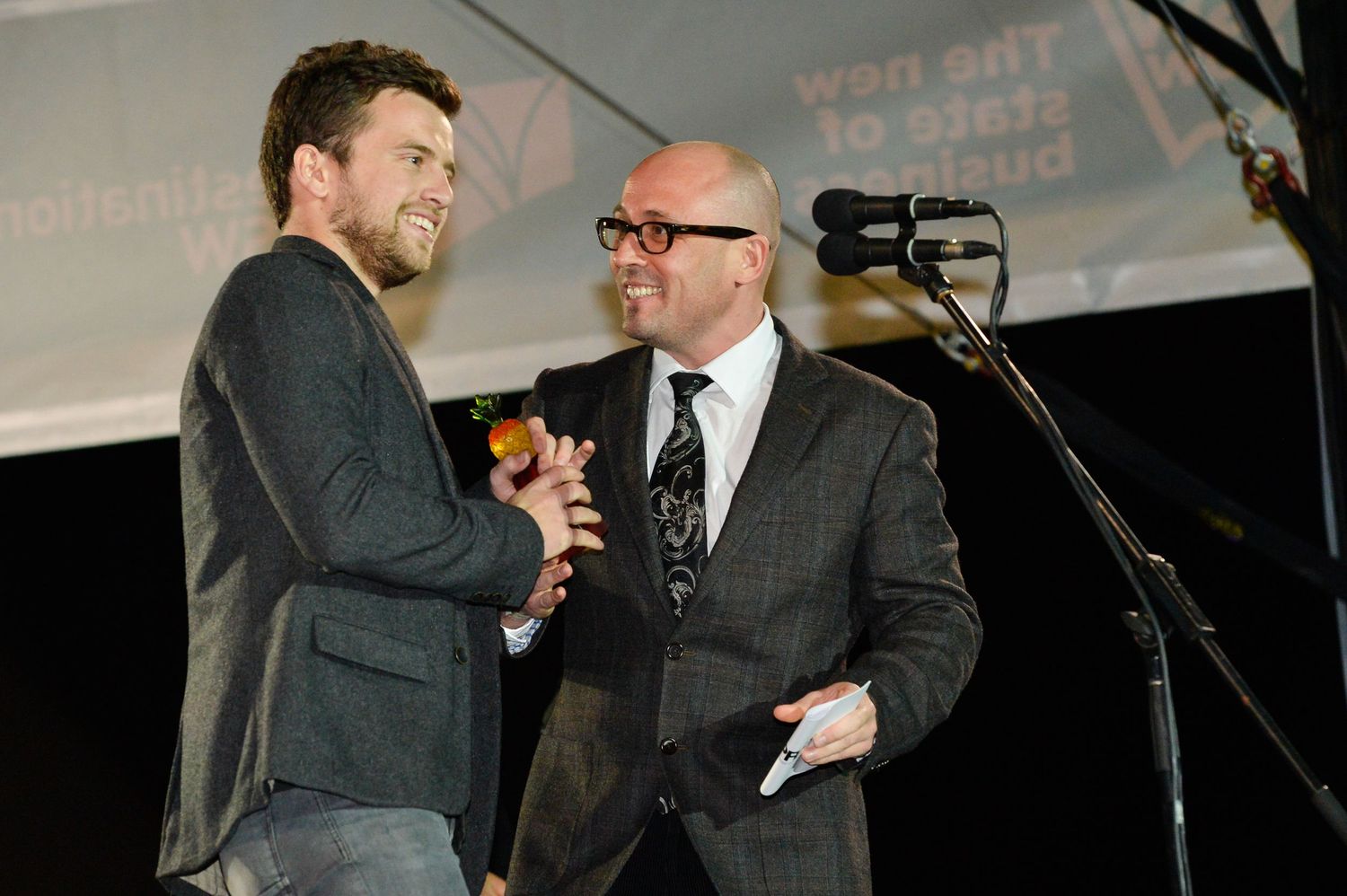 Two people in dark suits engage in animated conversation at what appears to be a formal event or gathering.