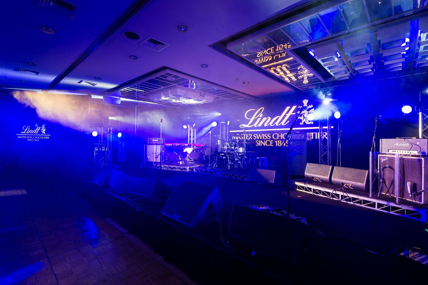 A dark concert venue with blue stage lighting illuminates multiple performance spaces and equipment setups.