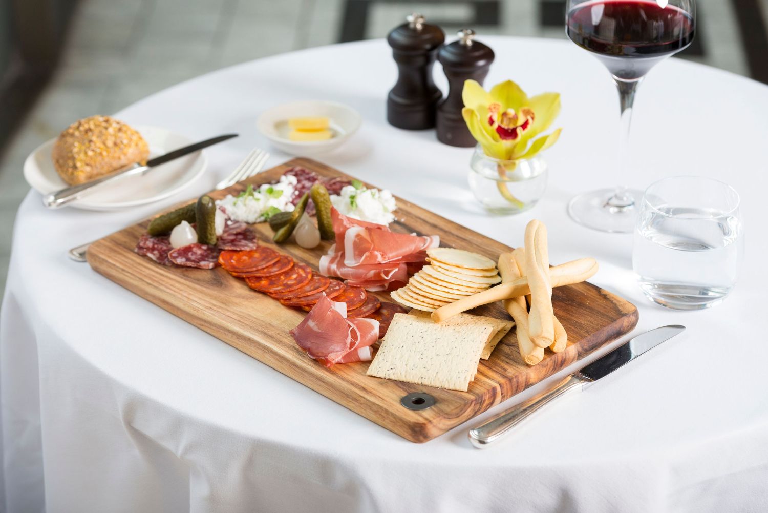 Fine dining table setting with wine glasses, charcuterie board, and yellow flower accents.
