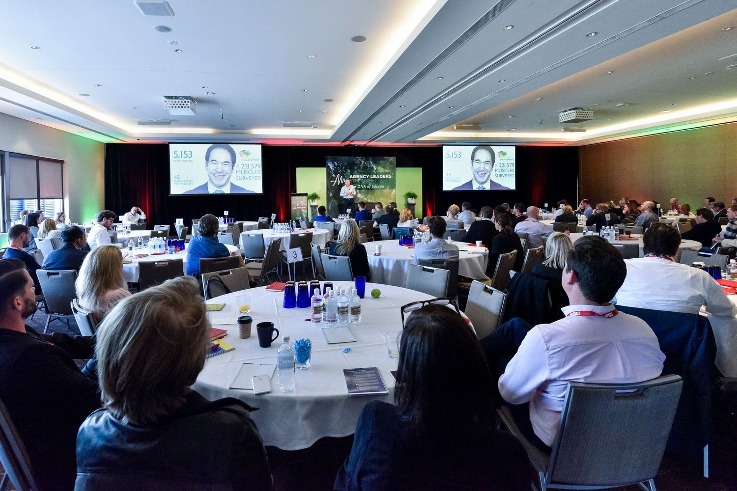 Large conference room filled with attendees watching a presentation on multiple screens.