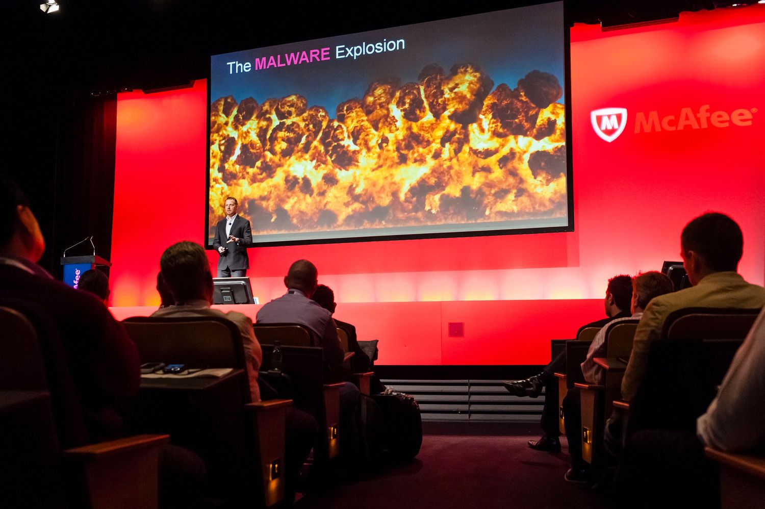 Wide conference stage setup with dramatic red lighting and presentation screens displaying security themes.