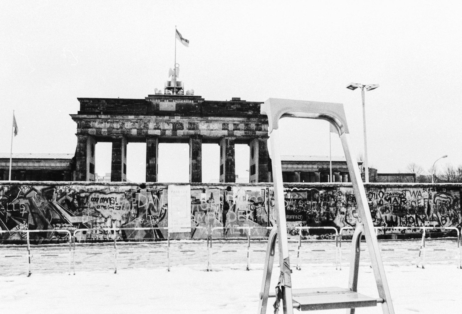 Black and white view of the Brandenburg Gate behind the Berlin Wall with a guard tower.