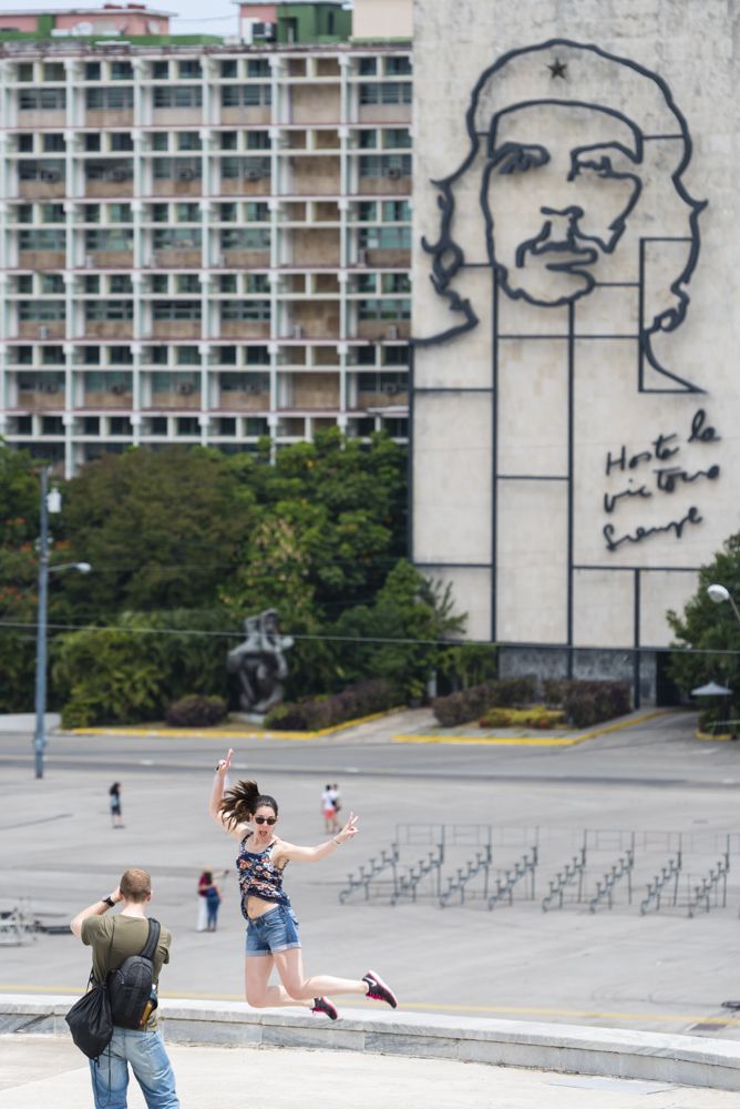 Female tourist while been photographed jumps in front of the iconic iron sculpture/mural in Plaza de la revolucion Havana Cuba.