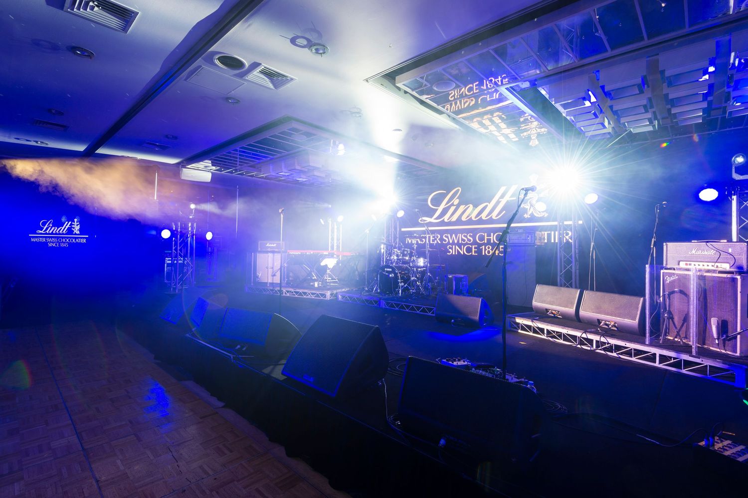 Blue stage lighting illuminates a dark concert venue with spotlights creating dramatic atmospheric effects.