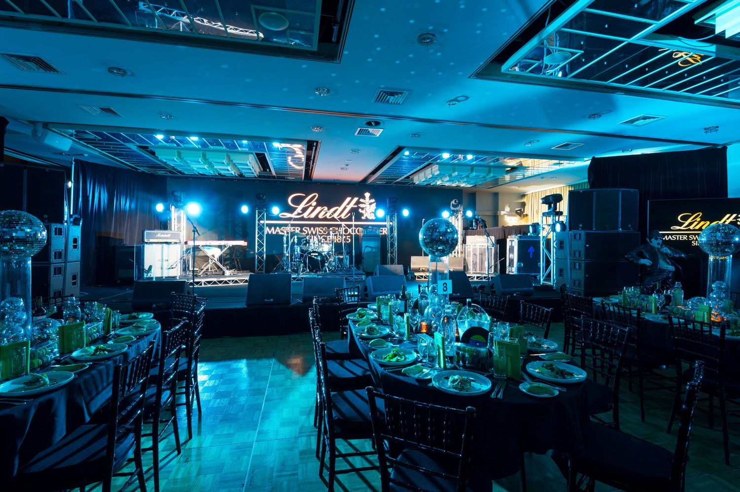 Elegant banquet hall illuminated in blue lighting with formal table settings and Lindt branding displayed on wall.