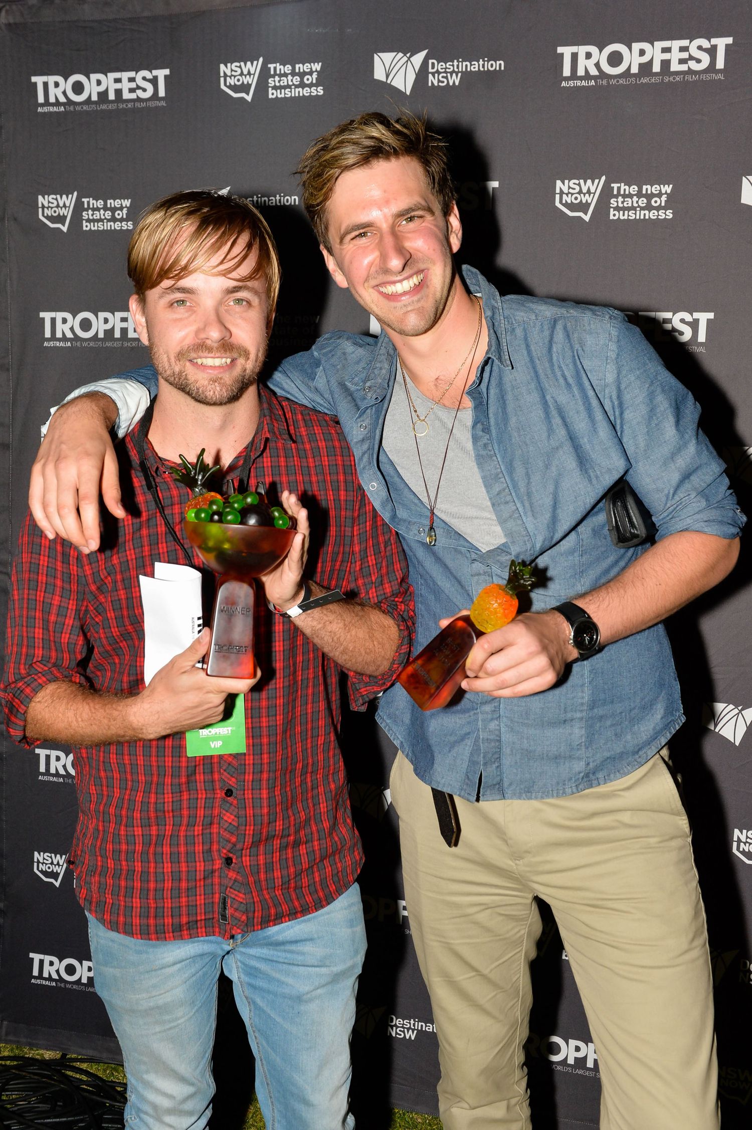 Two people pose together at the Tropfest film festival event against a dark backdrop with sponsor logos.