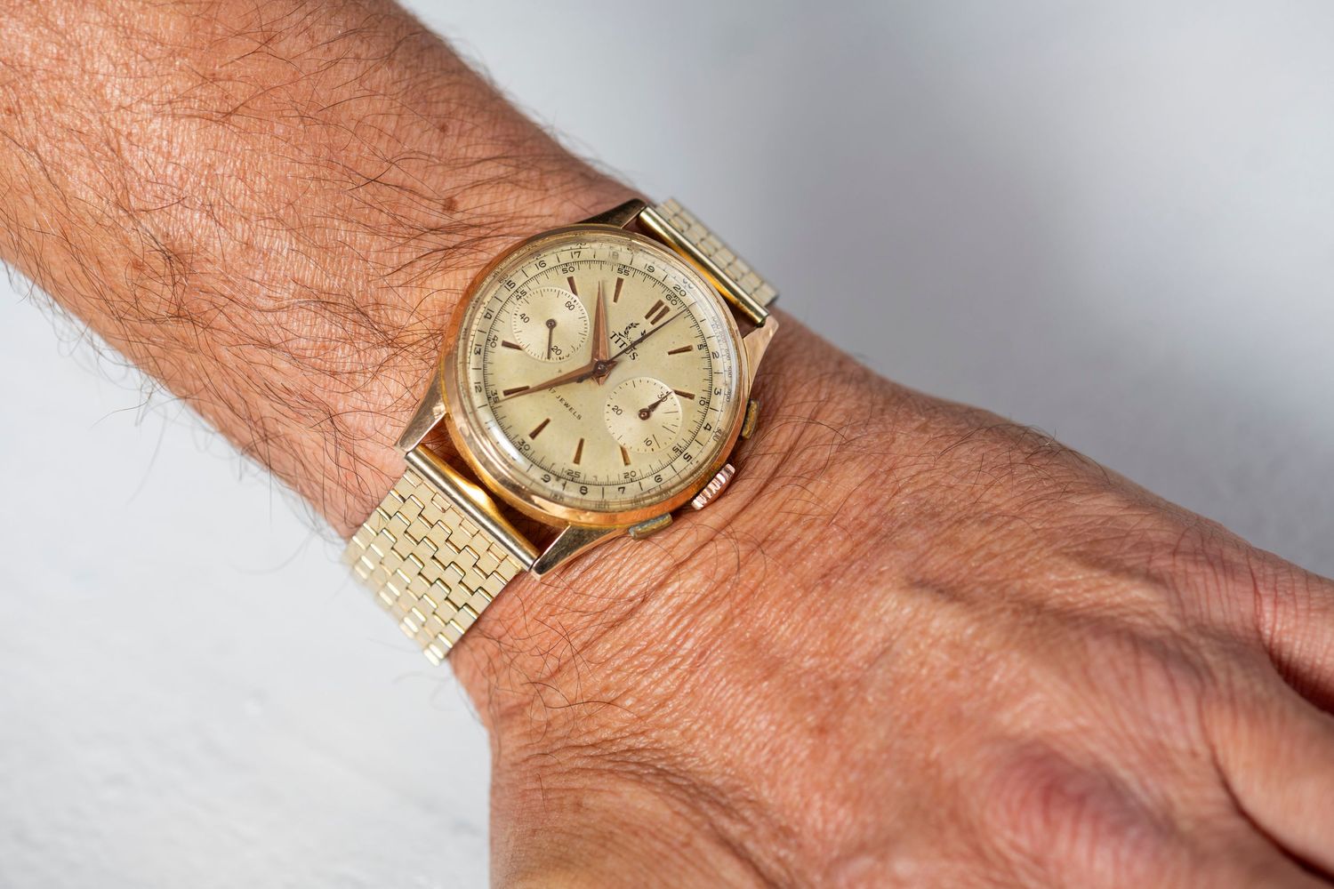 Gold vintage wristwatch with a champagne dial and mesh bracelet shown on someone's wrist.