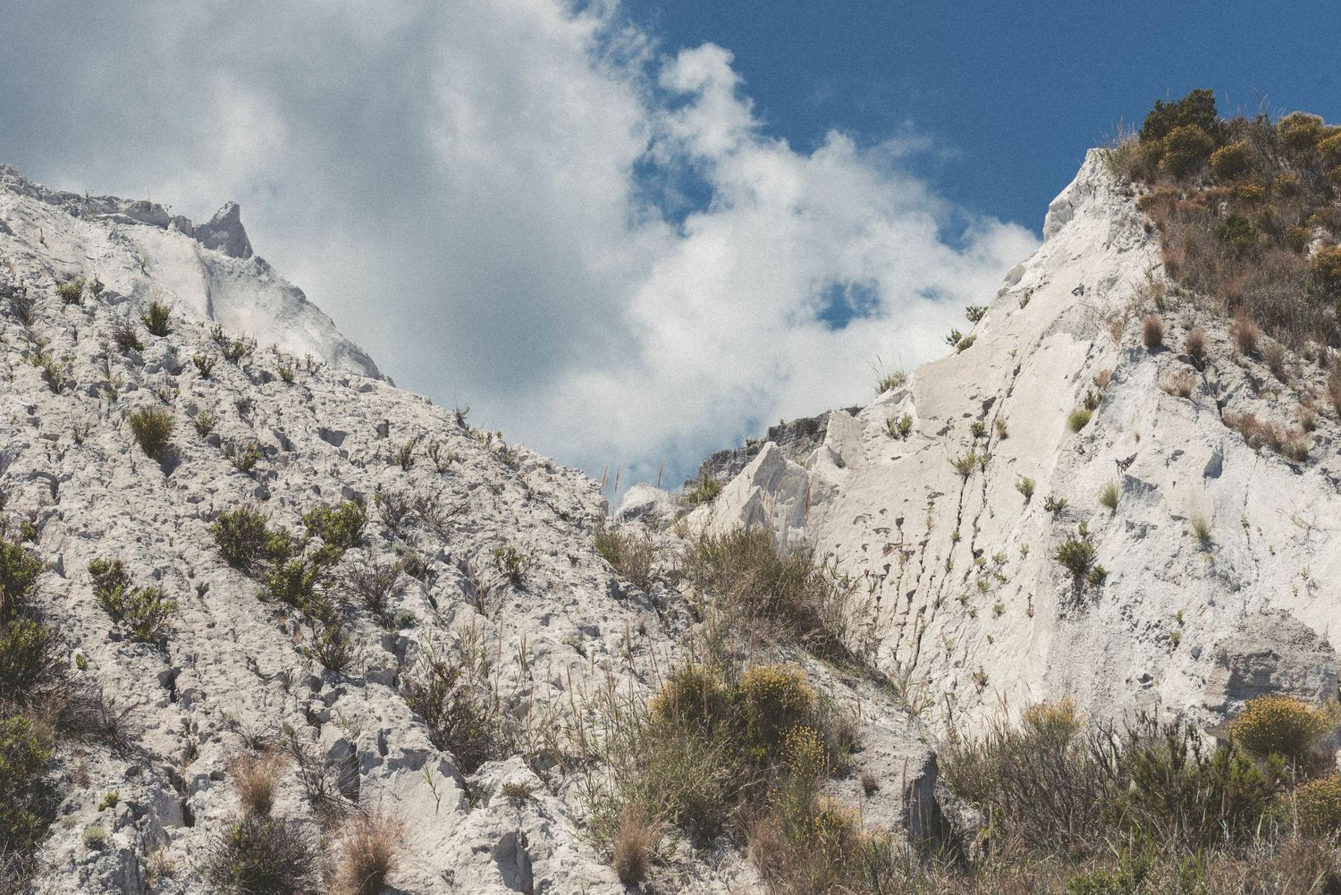 Panoramic view of white limestone cliffs and rocky mountain peaks against a cloudy blue sky.