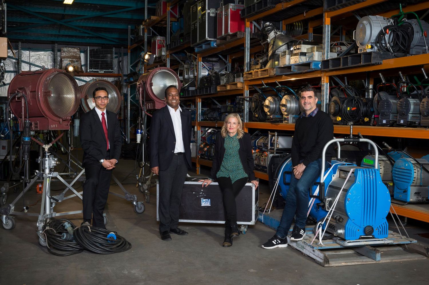 Group of people standing in a dimly lit warehouse or storage facility with equipment.