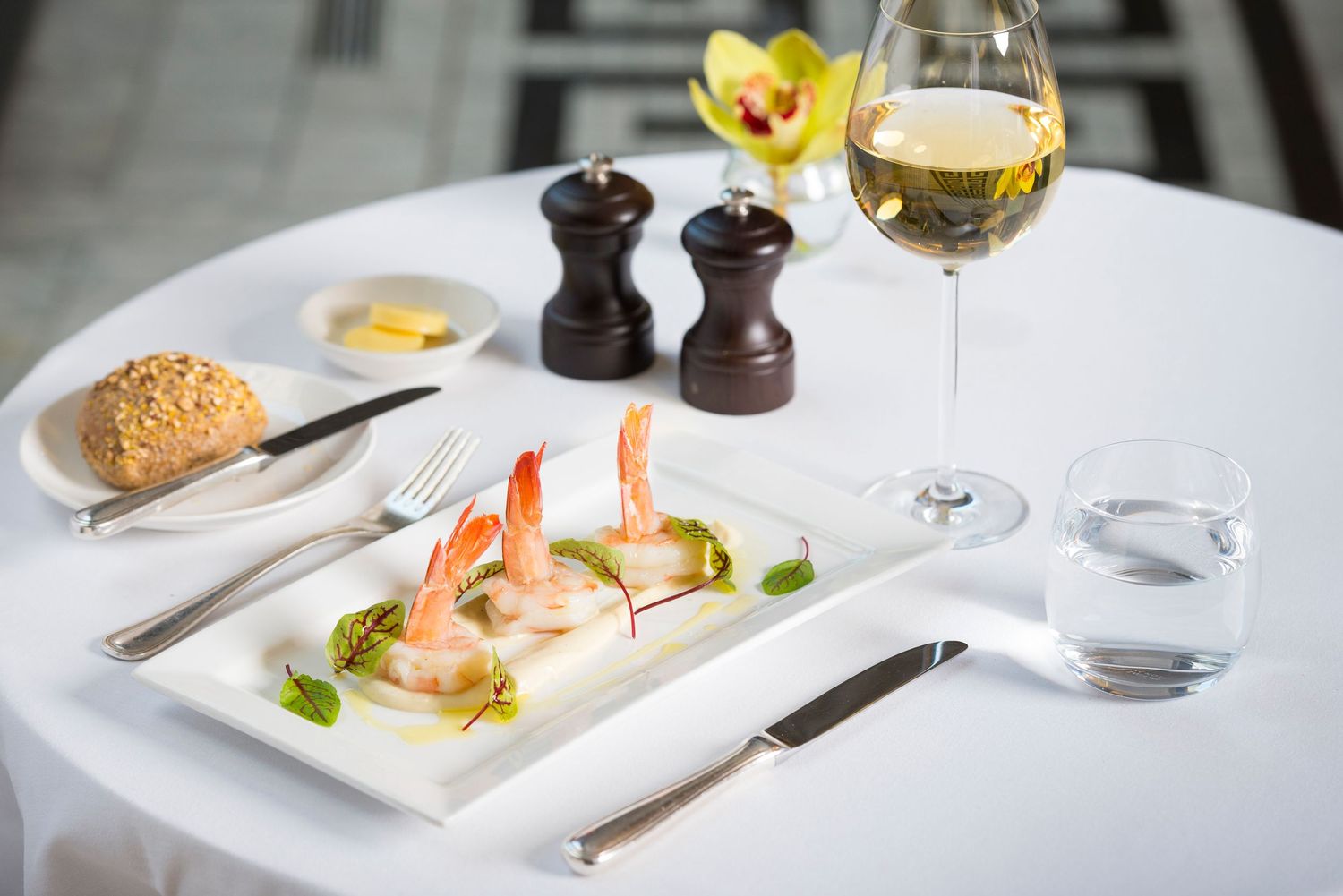 Upscale restaurant table setting with wine glasses, yellow flowers, and elegant plating.