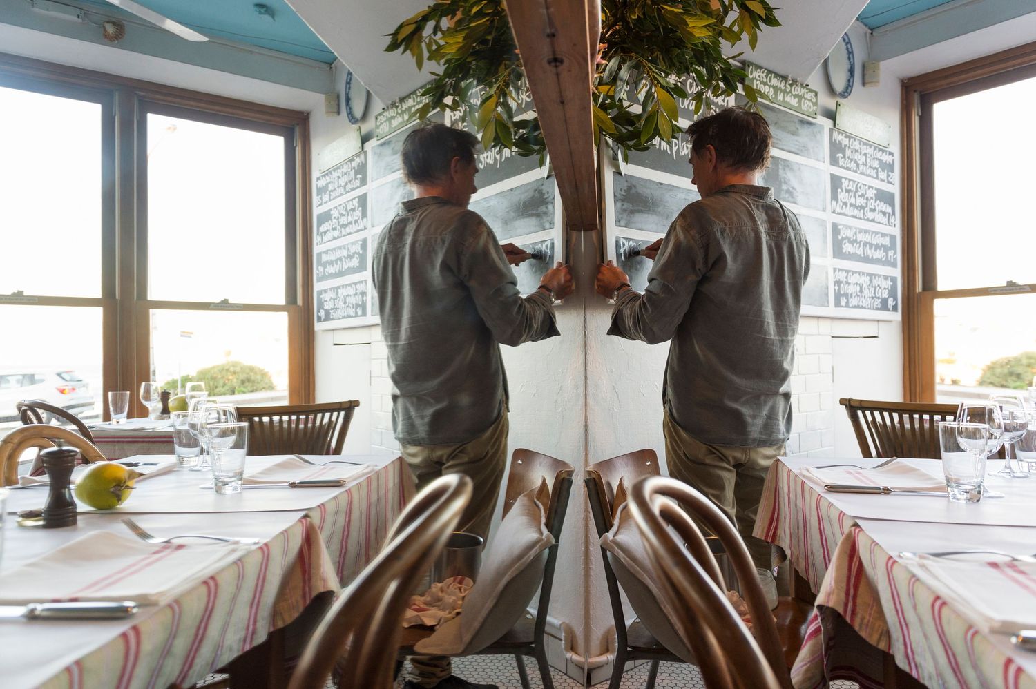 Diners enjoying a meal in a bright, modern restaurant interior with wooden chairs and large windows.
