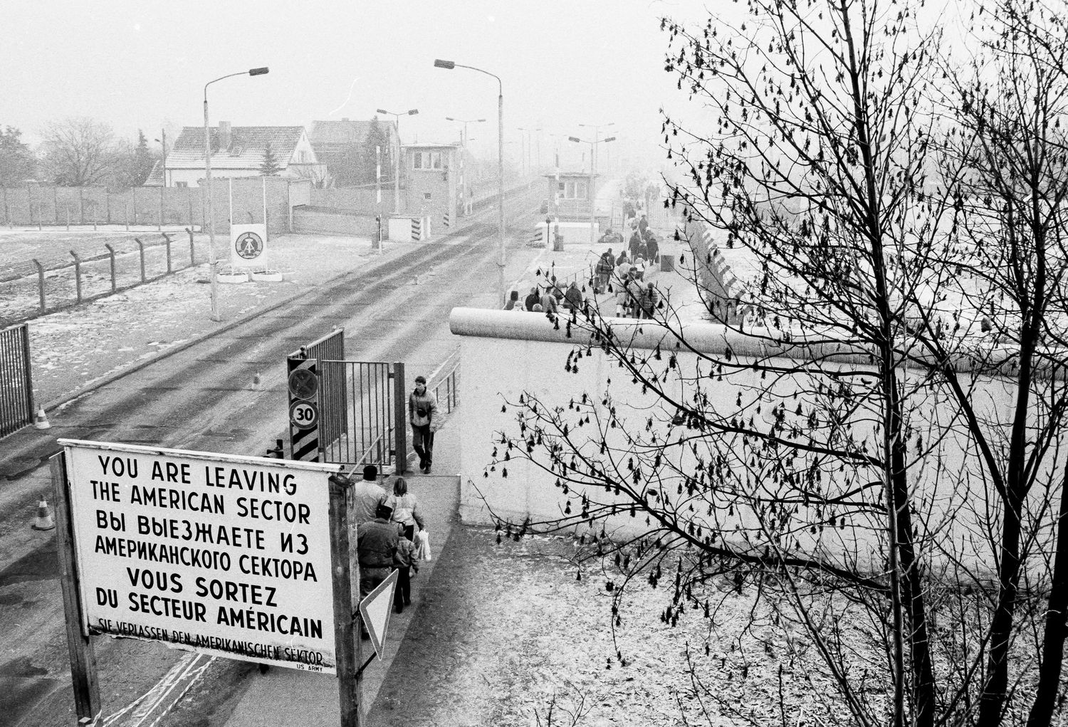 Foggy border crossing point with warning signs and barriers visible.