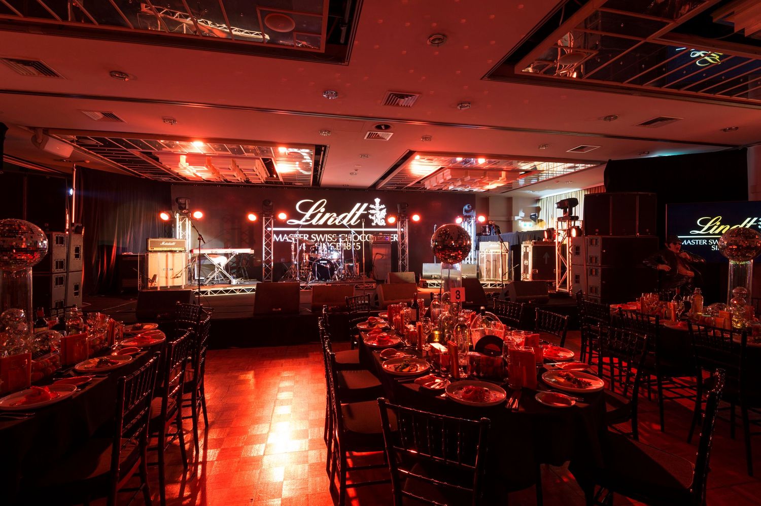 An elegant banquet hall with red ambient lighting and formal table settings beneath illuminated Lindt signage.