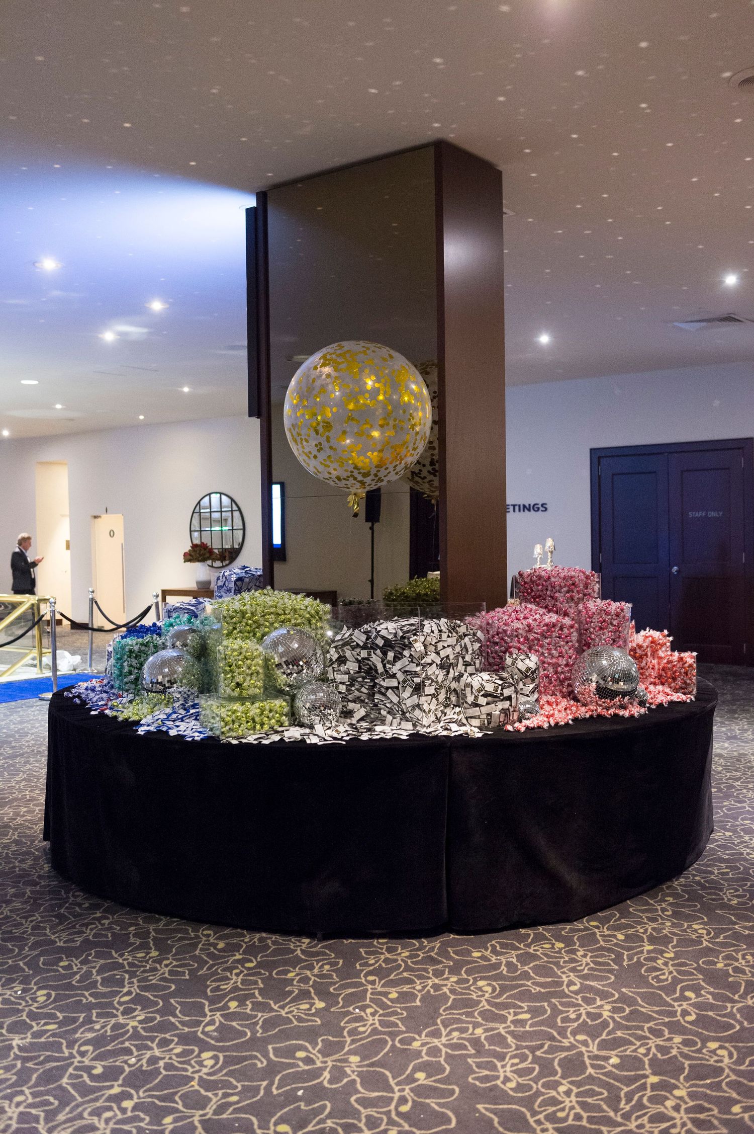 A panoramic view of a modern event space with black tables decorated with colorful balloon arrangements and floral displays.