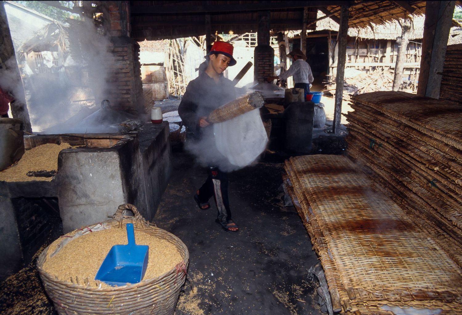 Traditional rice noodle making process showing steaming equipment and preparation in a rustic kitchen setting.