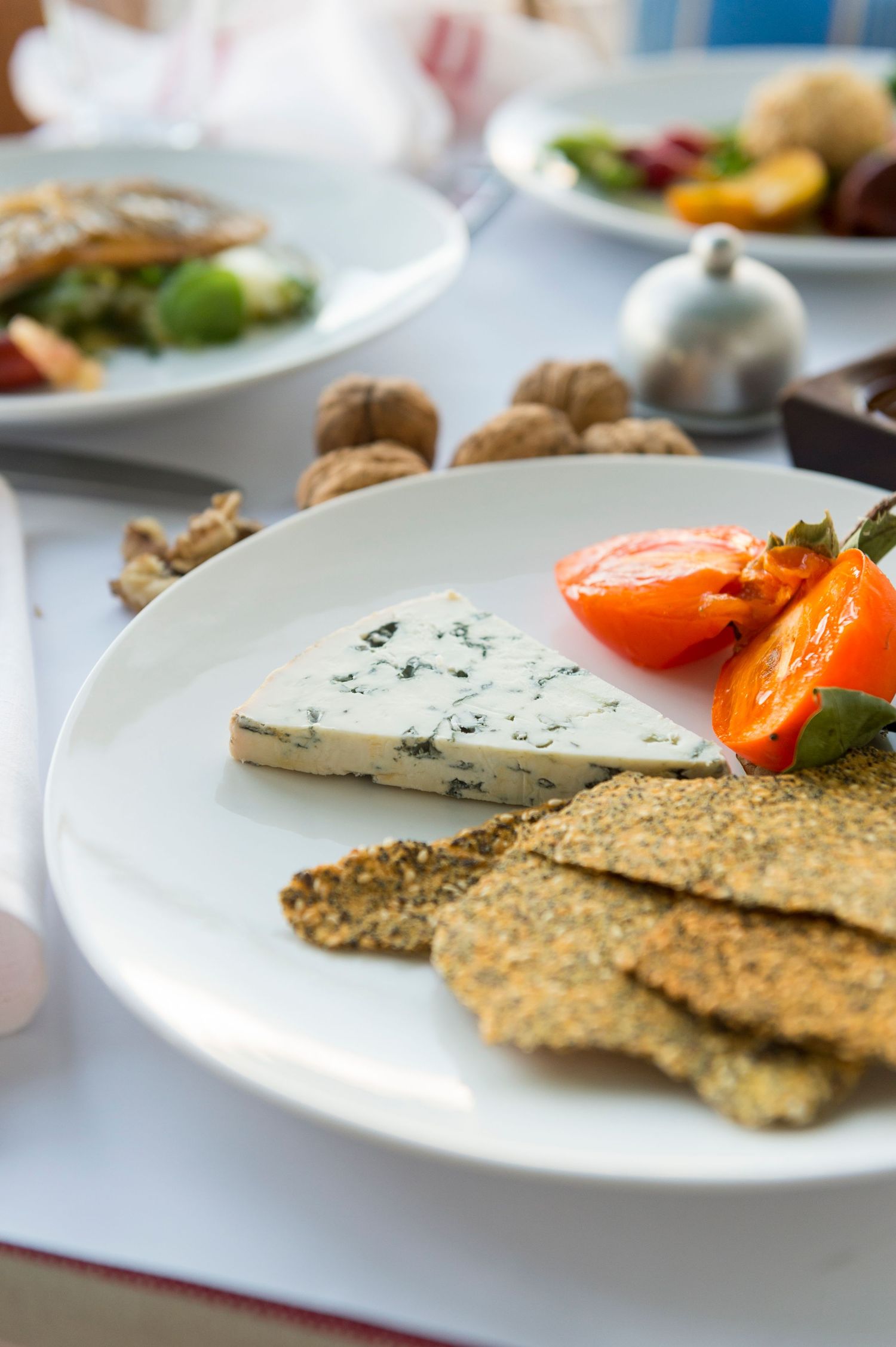 Artisanal crackers and blue cheese served with roasted apricots on white plates.