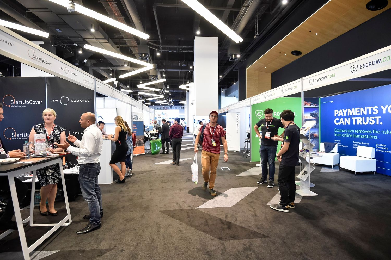 Trade show floor with various vendor booths and attendees networking in modern exhibition space.