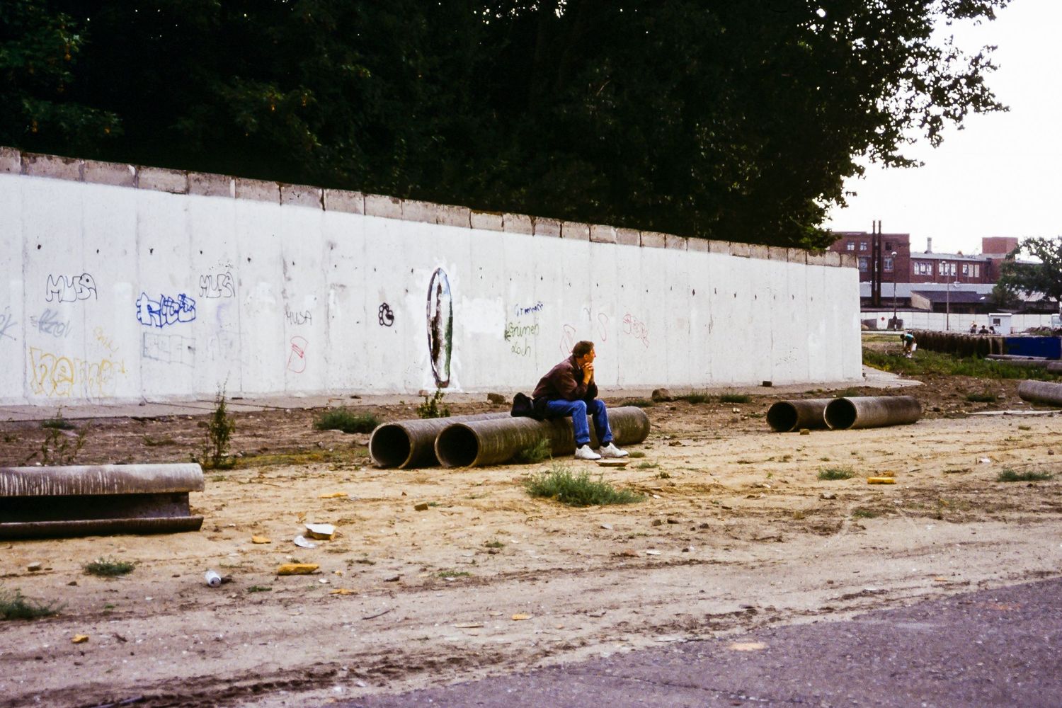 Solitary figure sits against a white wall with tires scattered on the ground.