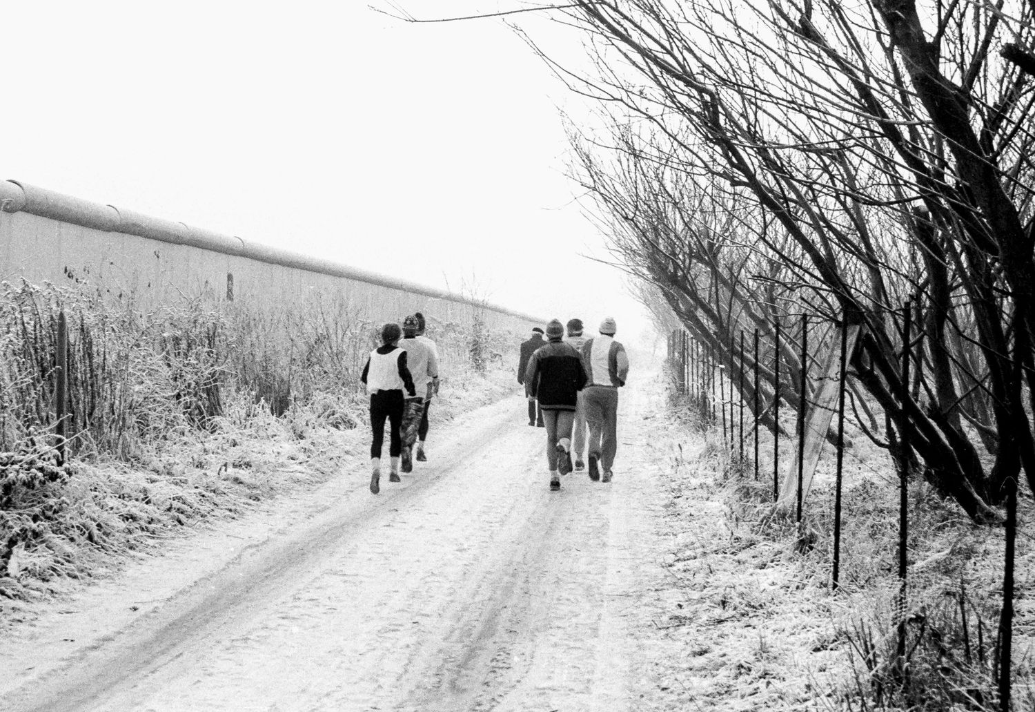 People walking along a snowy path next to the Berlin Wall.