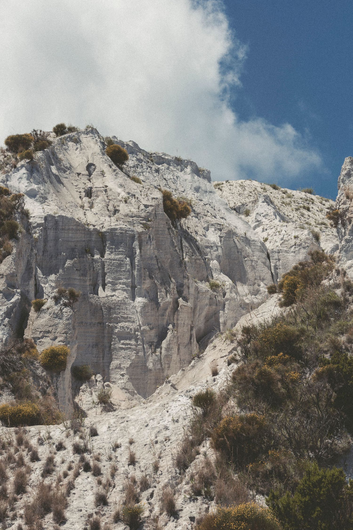 Dramatic white marble quarry cliffs with exposed rock faces against cloudy sky in Carrara, Italy.