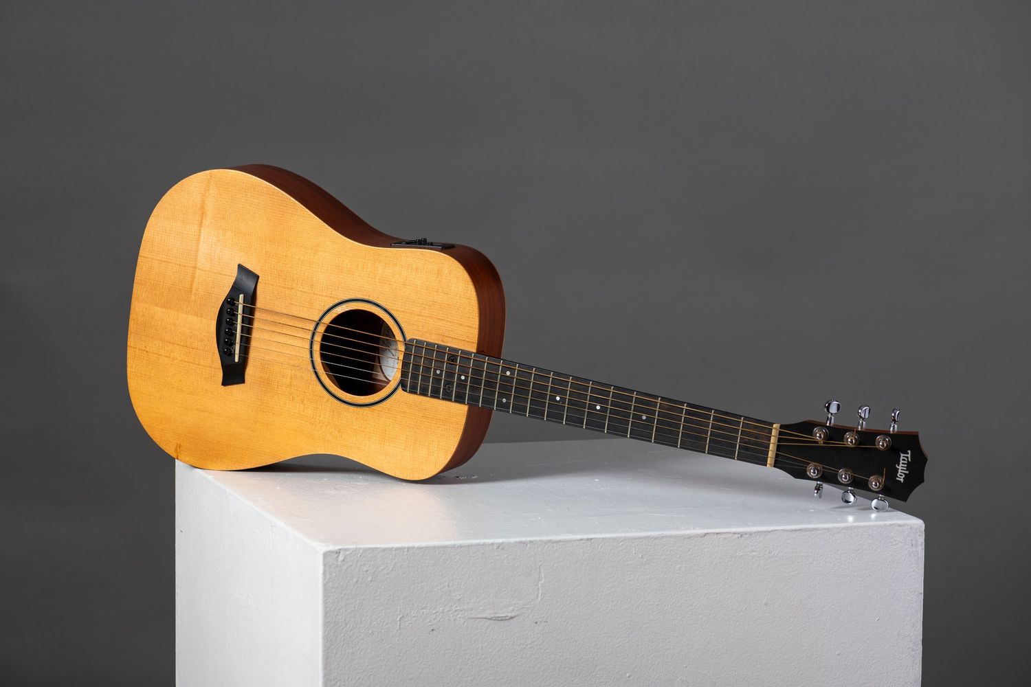A wooden acoustic guitar rests on a white surface with a clean minimalist composition.