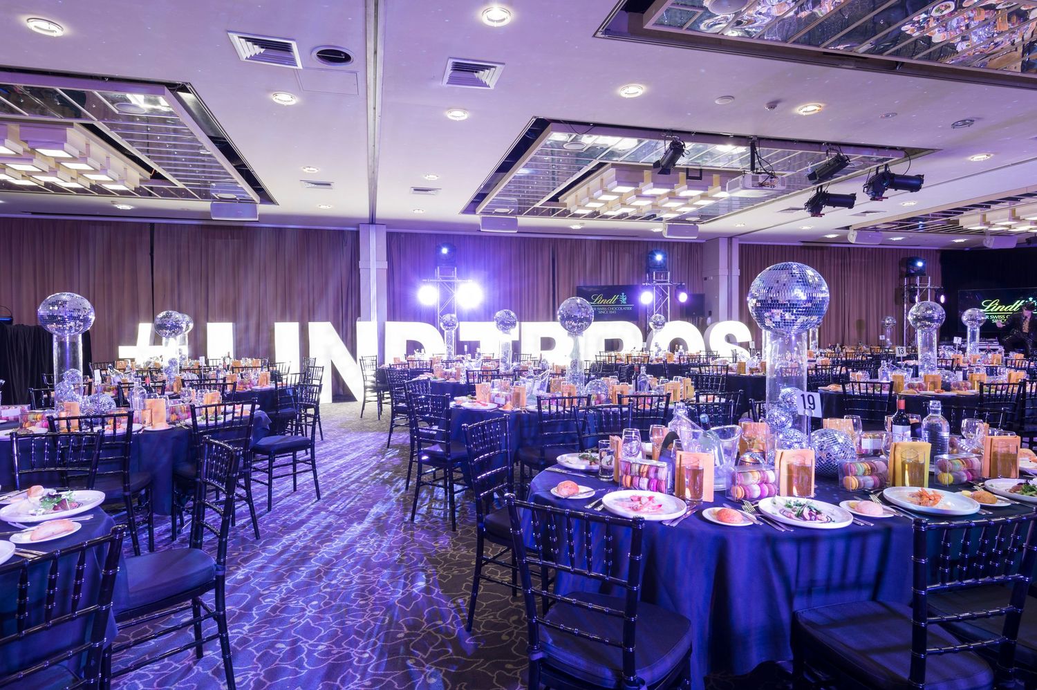 Panoramic view of an elegant banquet hall with blue uplighting and formal table settings for a special event.