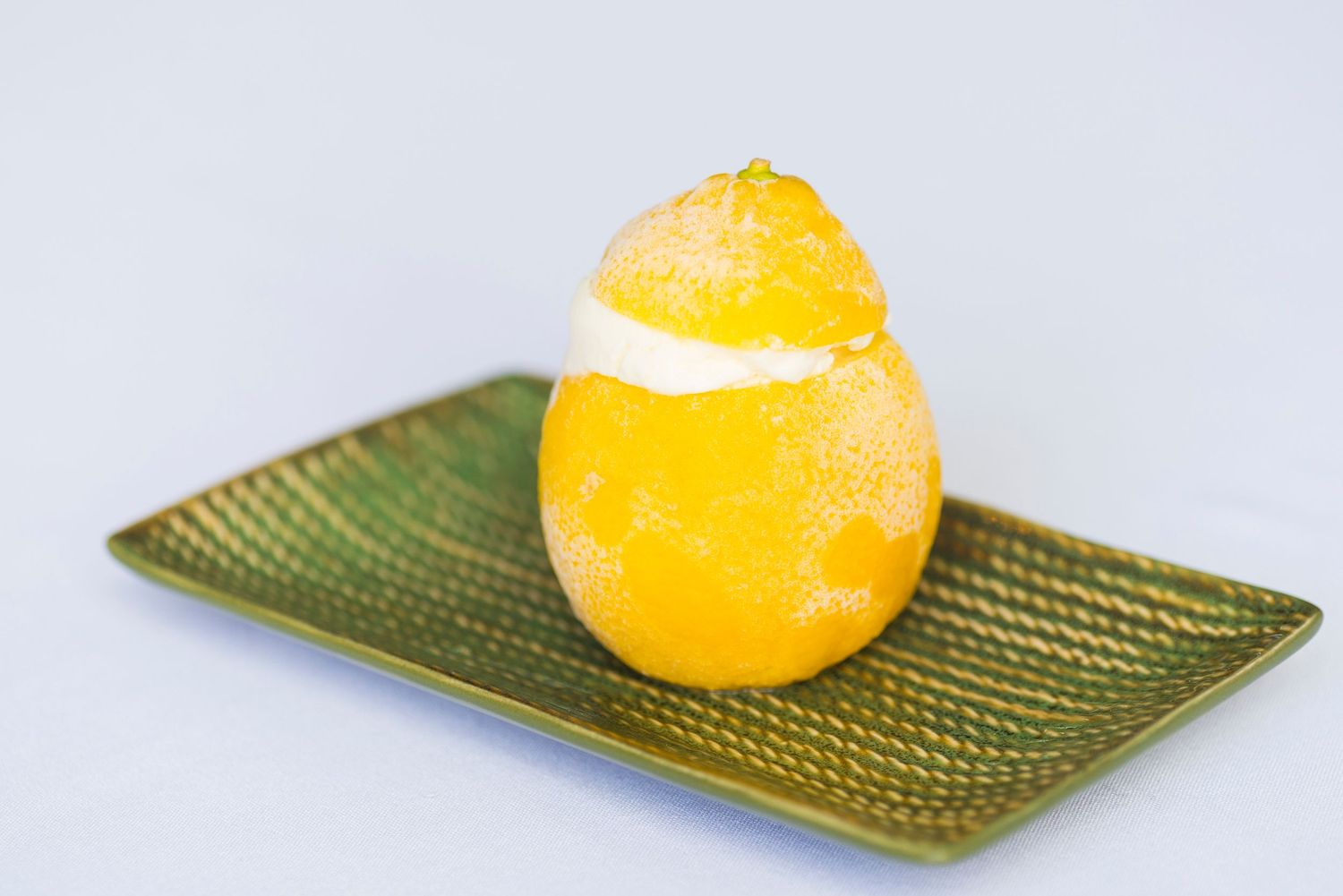 Citrus dessert with white cream stripe served on a textured green plate.