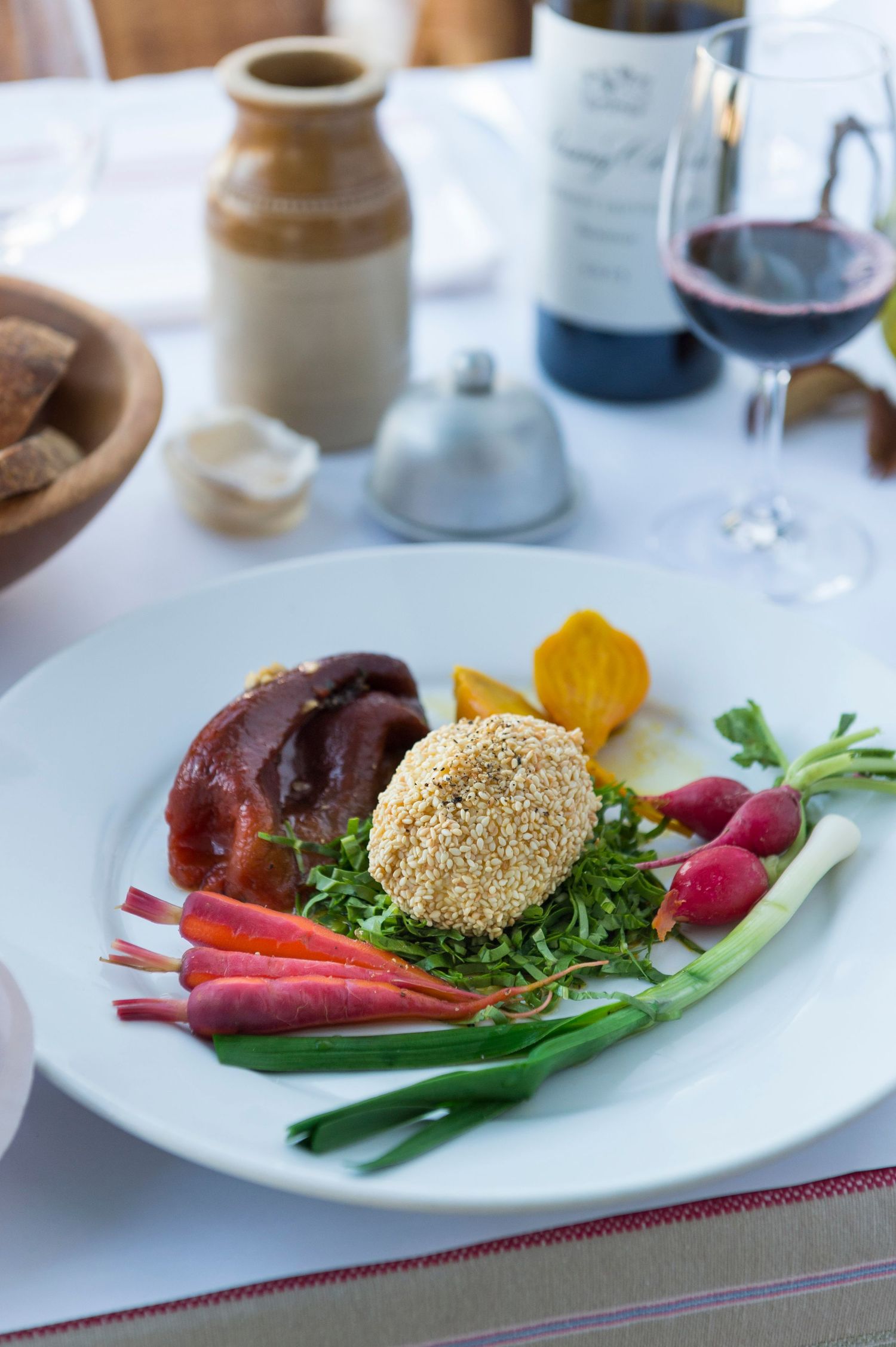 Beautifully plated dish with greens, radishes, and sesame-crusted item on white plate.