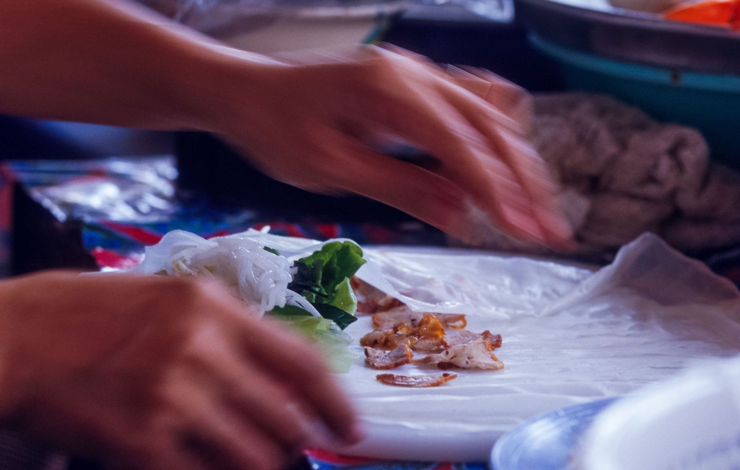 Close-up of hands preparing food ingredients at an Asian market stall.