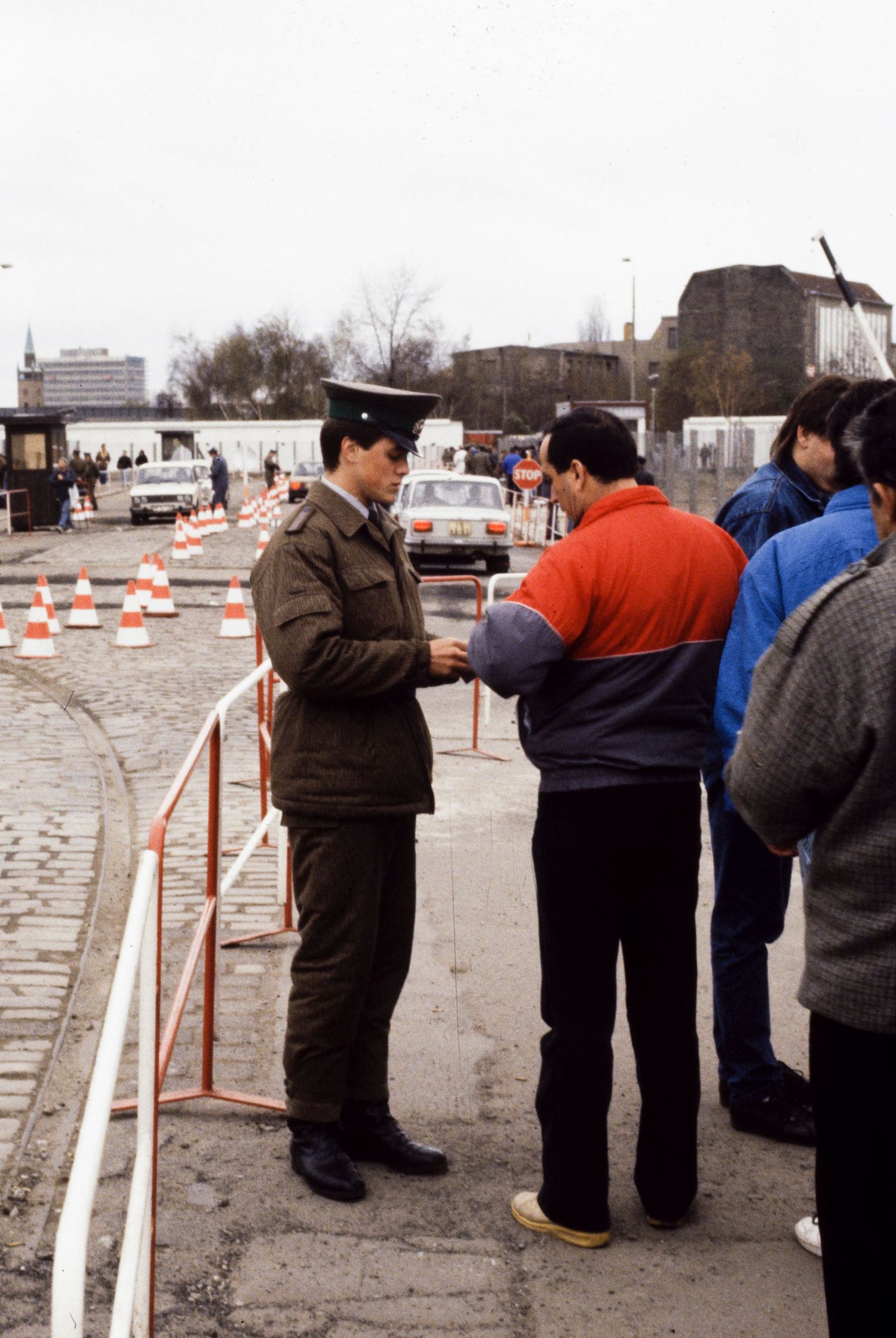 Border guards and civilians interact at a checkpoint barrier in East Berlin.