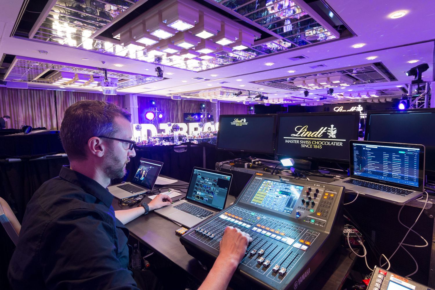 Professional audio mixing console with purple lighting in a recording studio control room setup.