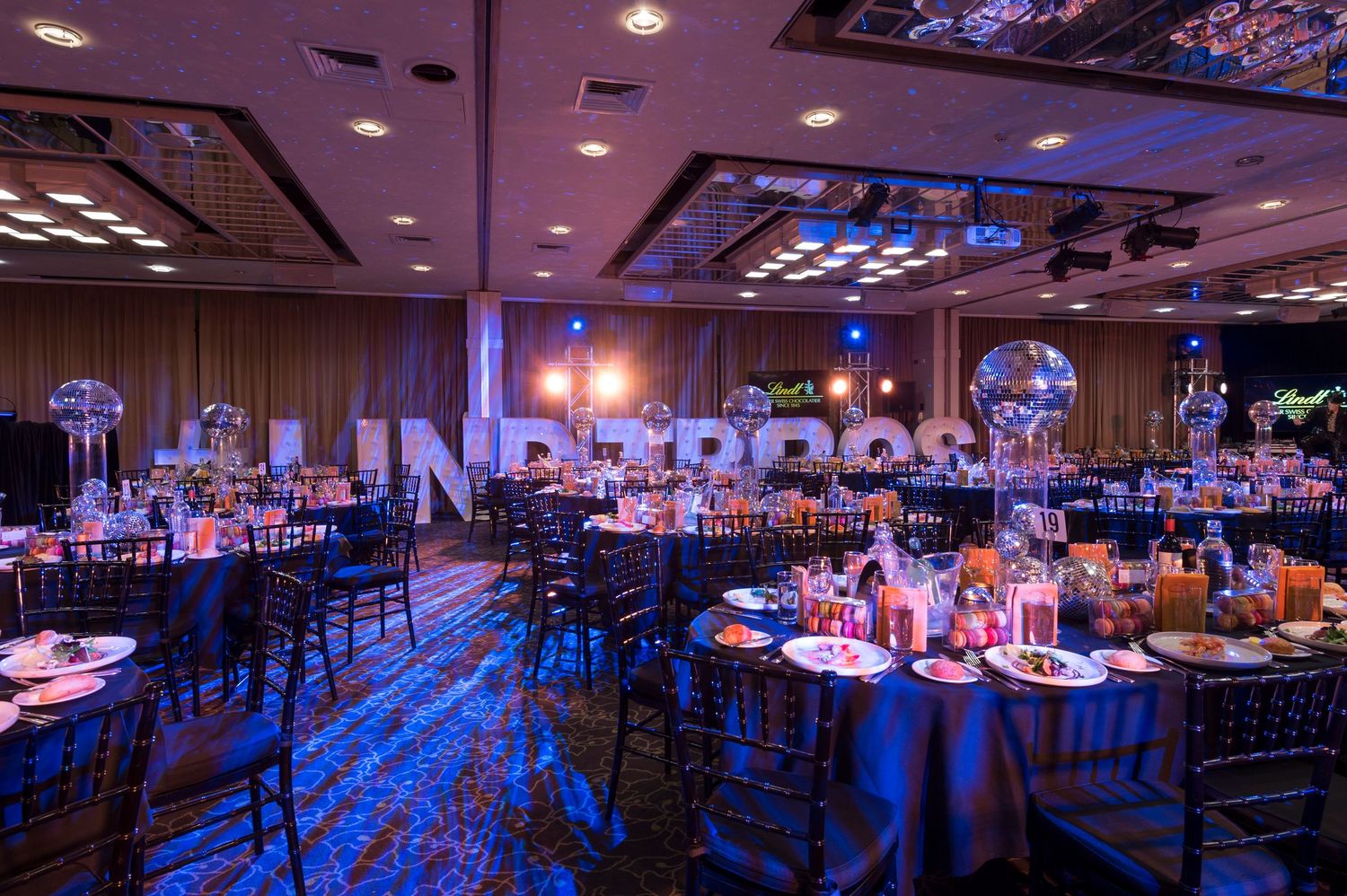 A large banquet hall decorated with blue uplighting and elegant table settings for a formal event.