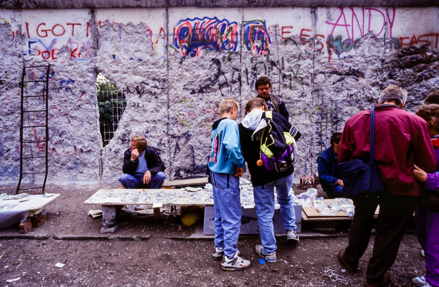 Group of people gathered near a graffiti-covered wall with benches in an urban setting.