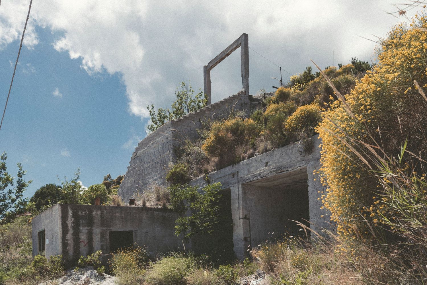 Abandoned concrete bunker with metal frame structure on hilltop against blue sky with white clouds.
