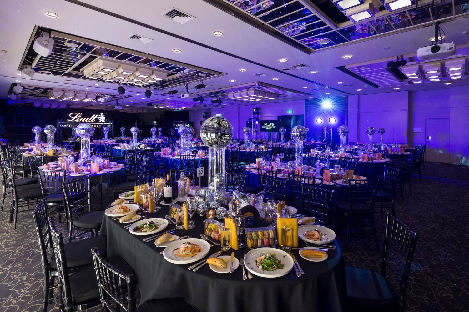 Elegant banquet hall setup with blue uplighting illuminating tables set for a formal dinner service.
