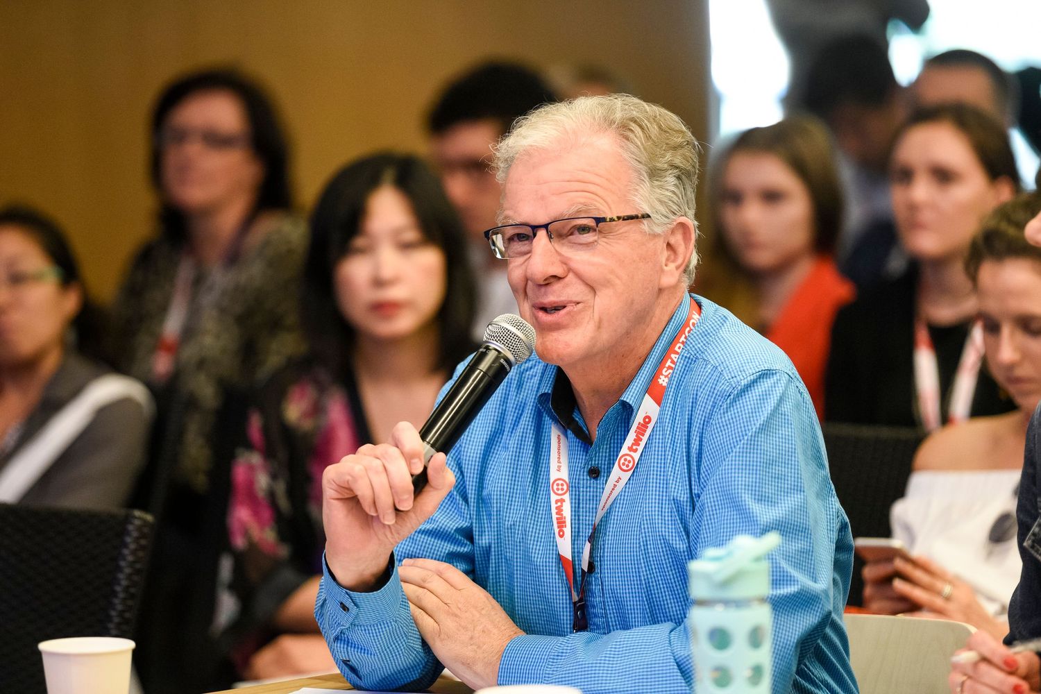 Conference participant in blue shirt speaks into microphone during interactive session.