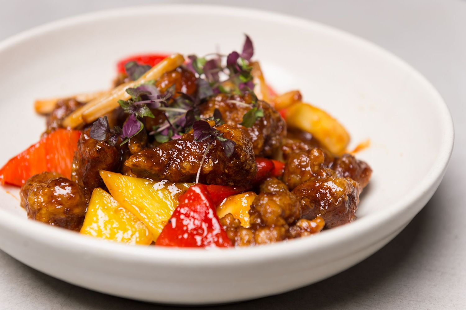 Colorful sweet and sour dish with bell peppers and sauce on white plate.