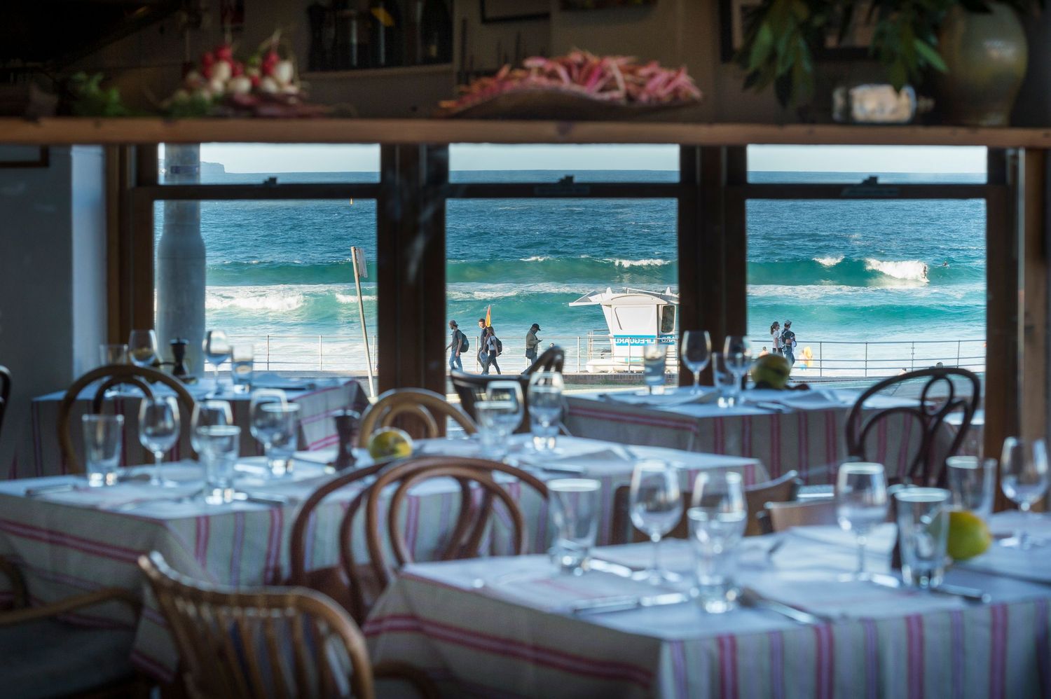 Elegant restaurant dining room with ocean views through large windows and white tablecloths on tables.